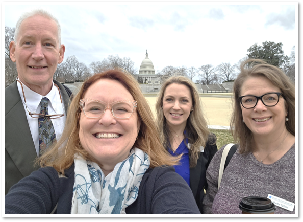 Group of four people - one man and three women - standing outside taking a picture of themselves.