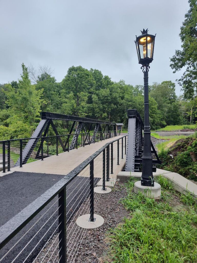 Paved walkway across bridge with guardrails and light post.