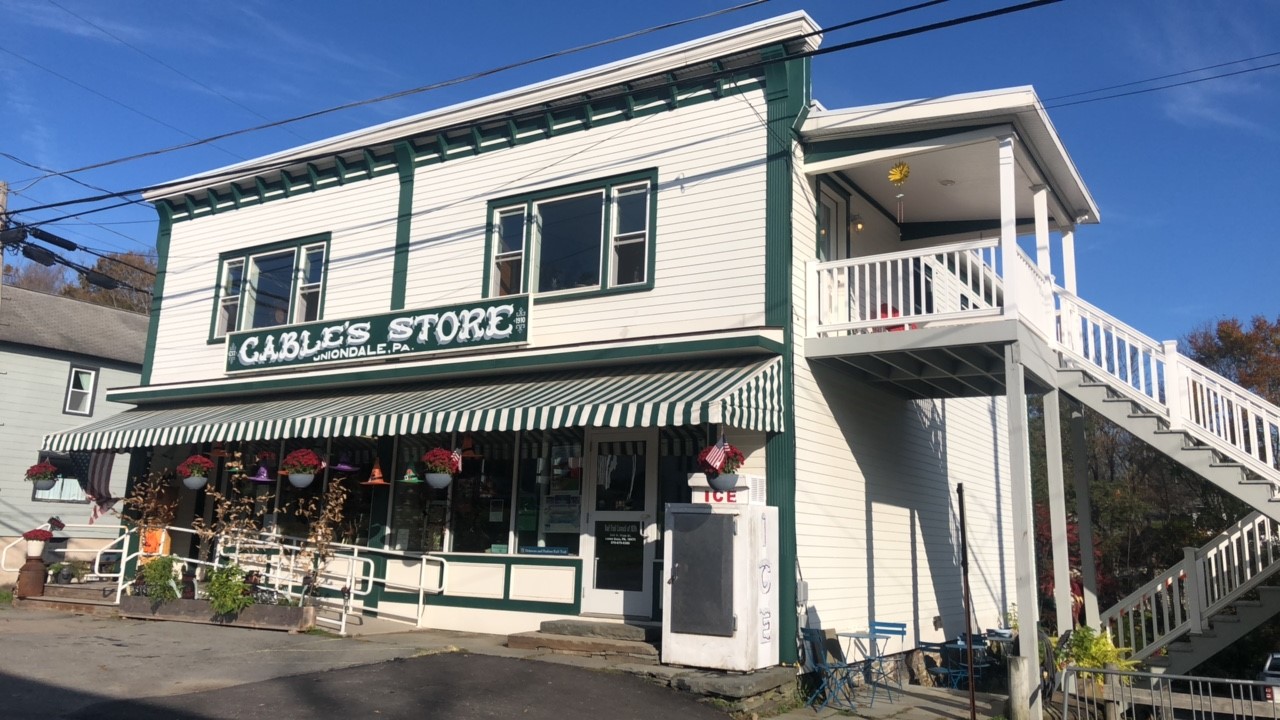 Two story wood frame story with first floor storefront, colorful awning, and stair to second floor porch.