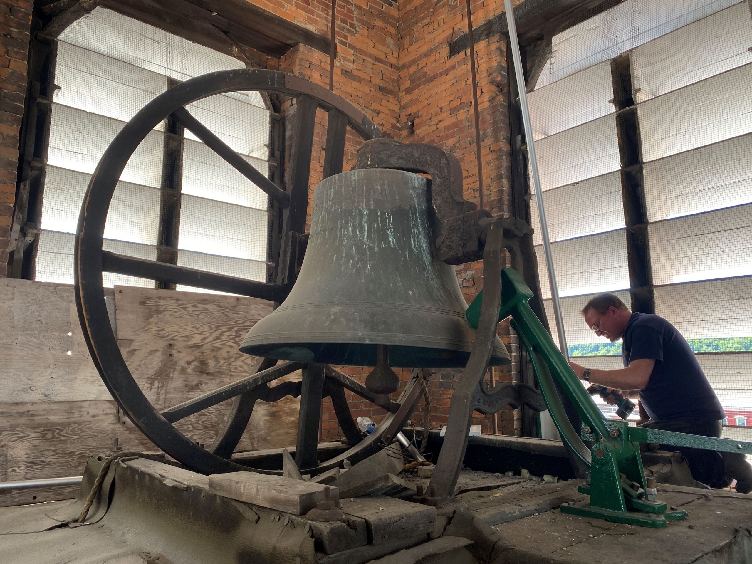 Man works with power drill next to large bell and gears inside a brick church steeple.