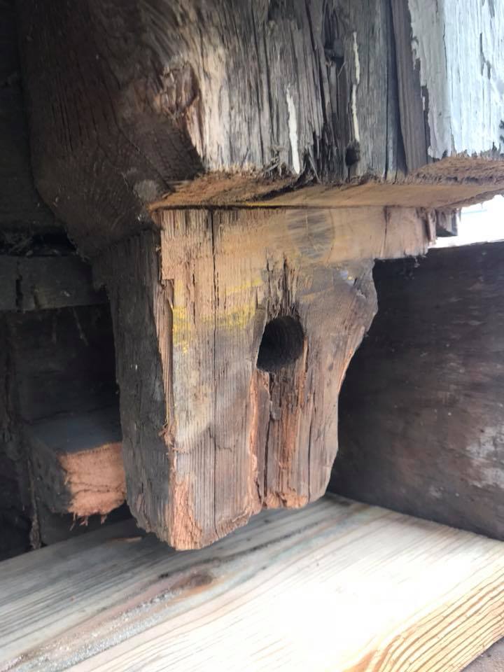 End of wood beam with hole in center showing deterioration.