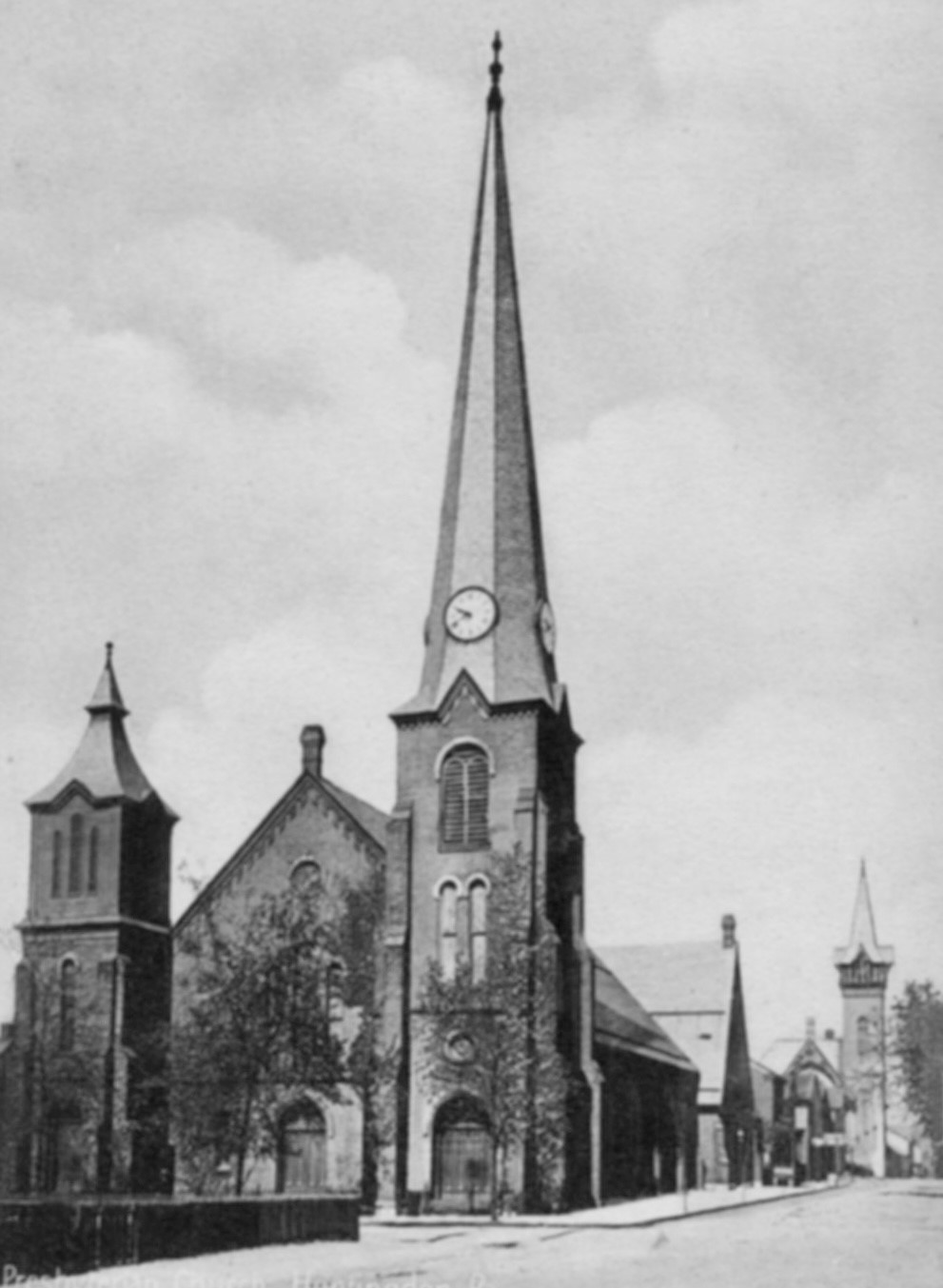 Brick church at intersection of two streets with a very tall corner steeple.