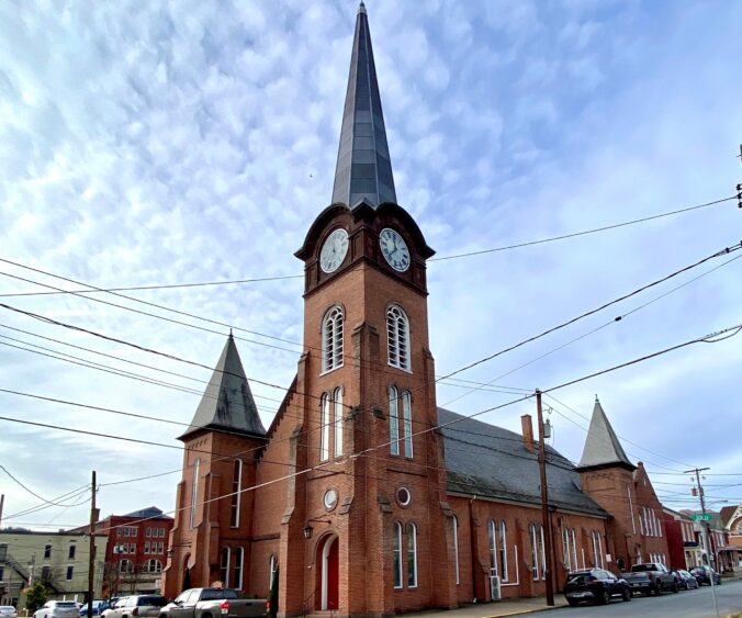 Brick church at an intersection of two streets with a tall corner steeple.