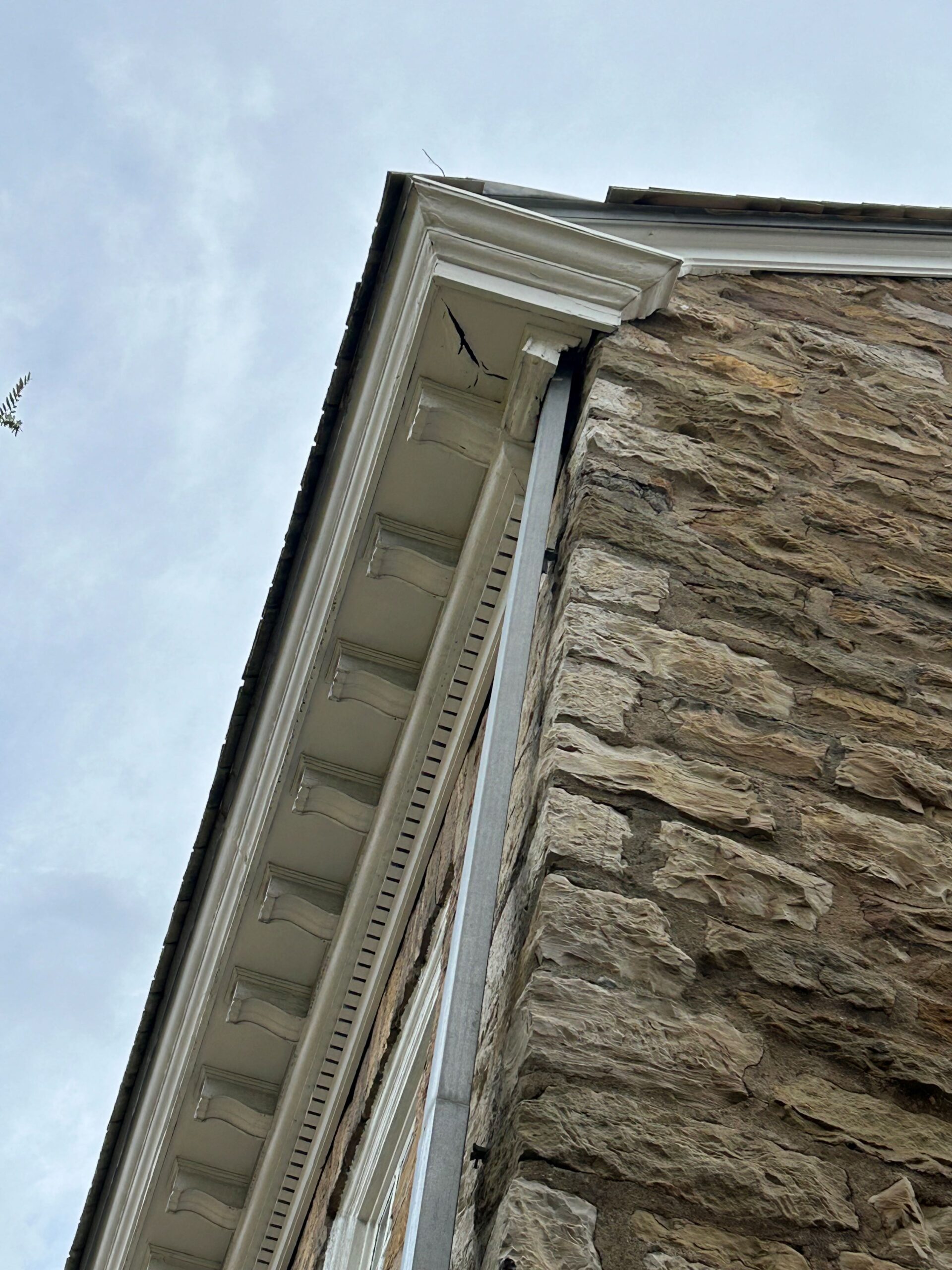 Detail of a wood building cornice at the top of a stone wall.