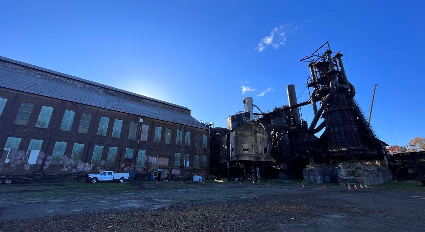 Industrial property with paved lot, large brick building with boarded up windows, and large metal structures.
