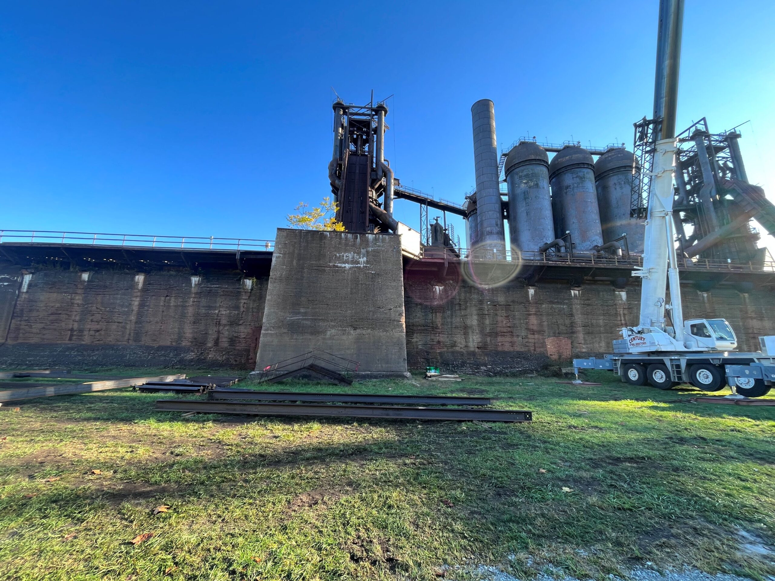 Tall concrete wall with many large steel stacks and crane.