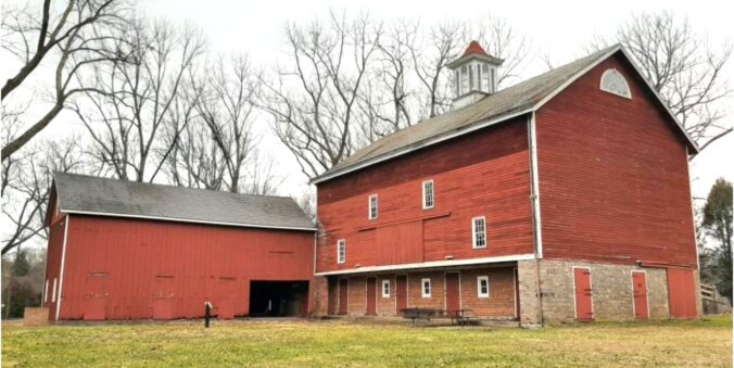 Large three-story wood and stone barn with two story wood building at a right angle to the back corner.