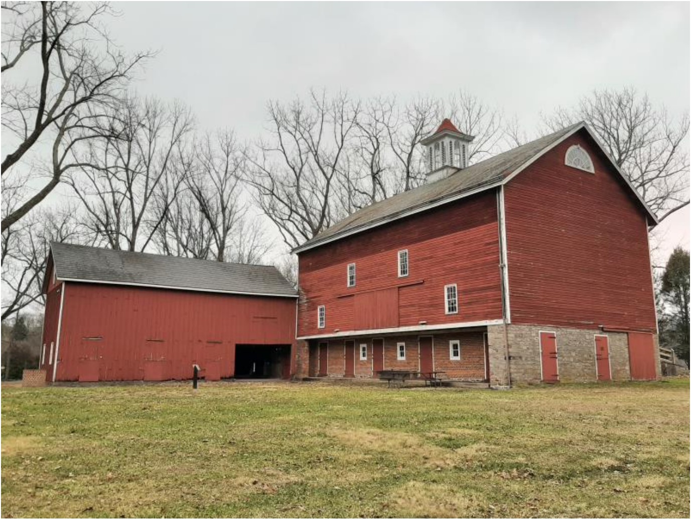Large three-story wood and stone barn with two story wood building at a right angle to the back corner.