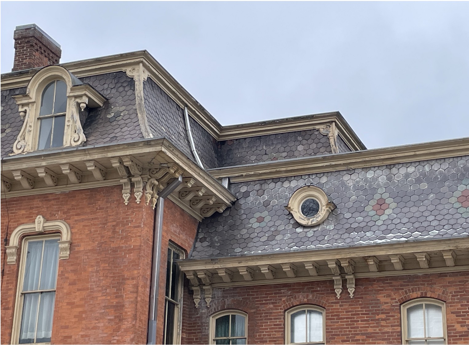 Decorative hexagonal slate shingles on the sides of a roof over a brick building.
