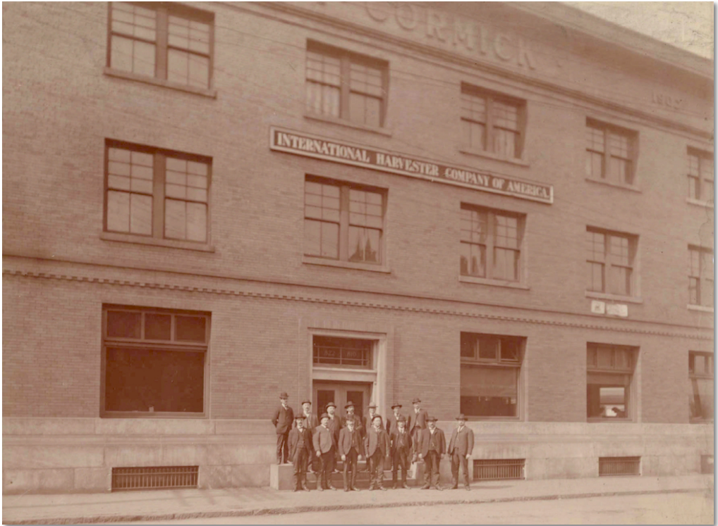 Sepia image of a group of men standing in front of a large brick building.