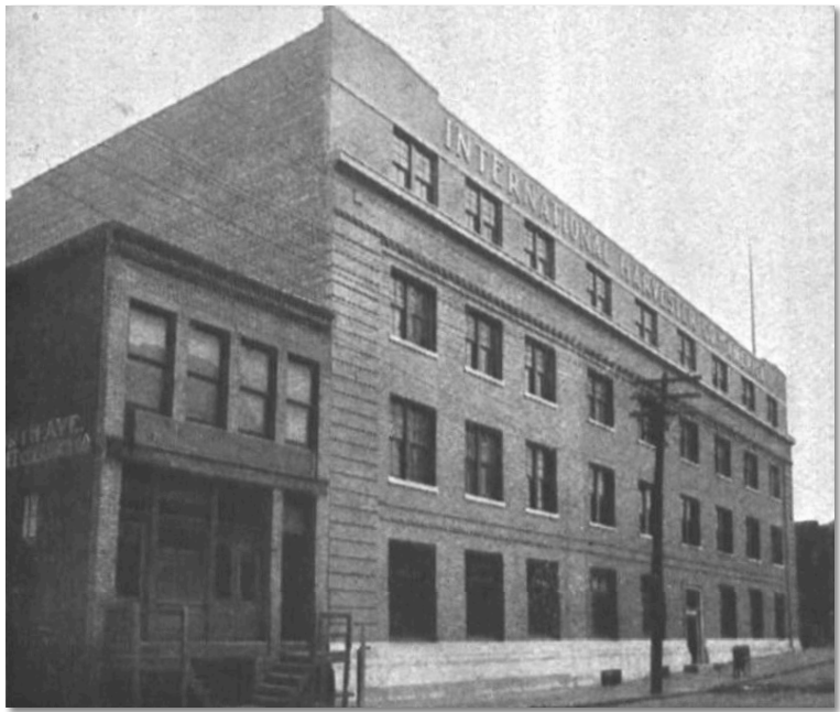 Black and white image of large 4-story brick building with many windows along each floor in an urban setting.