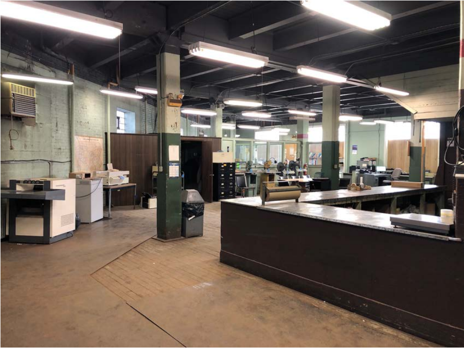 Large, unfinished office space with desk, wood floors, and office machinery.