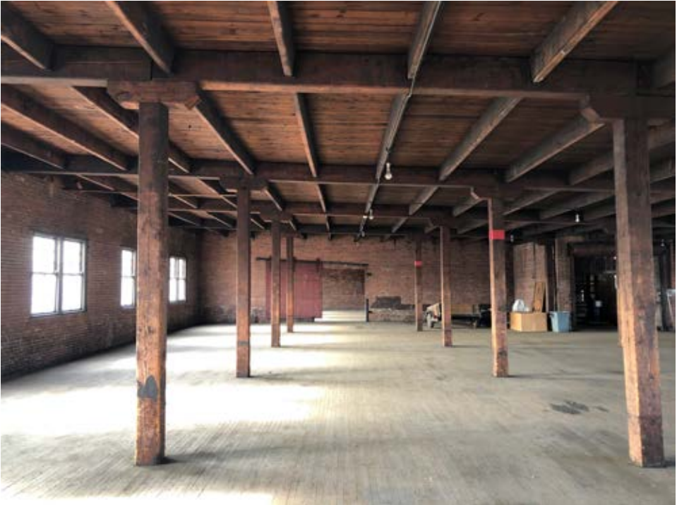 Large, open unfinished floor space punctuated by evenly-placed wood columns, open wood ceiling, and unpainted brick walls.
