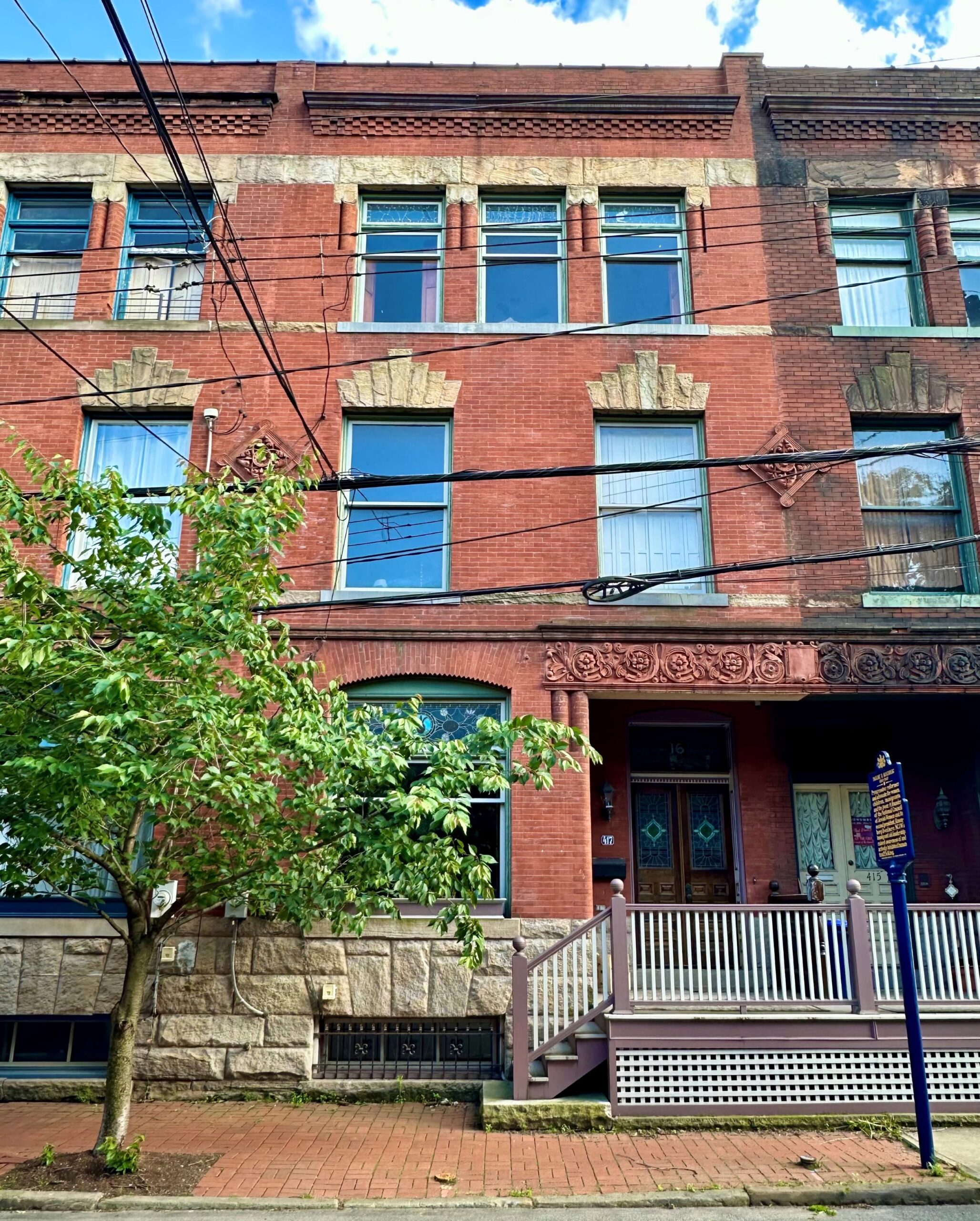 Three story residential brick rowhouse with a tree and marker in front of building.