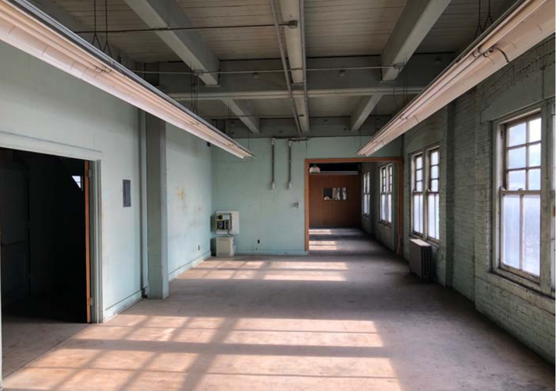 Open rectangular space with painted brick wall and windows to the right and openings to another space at front and left.
