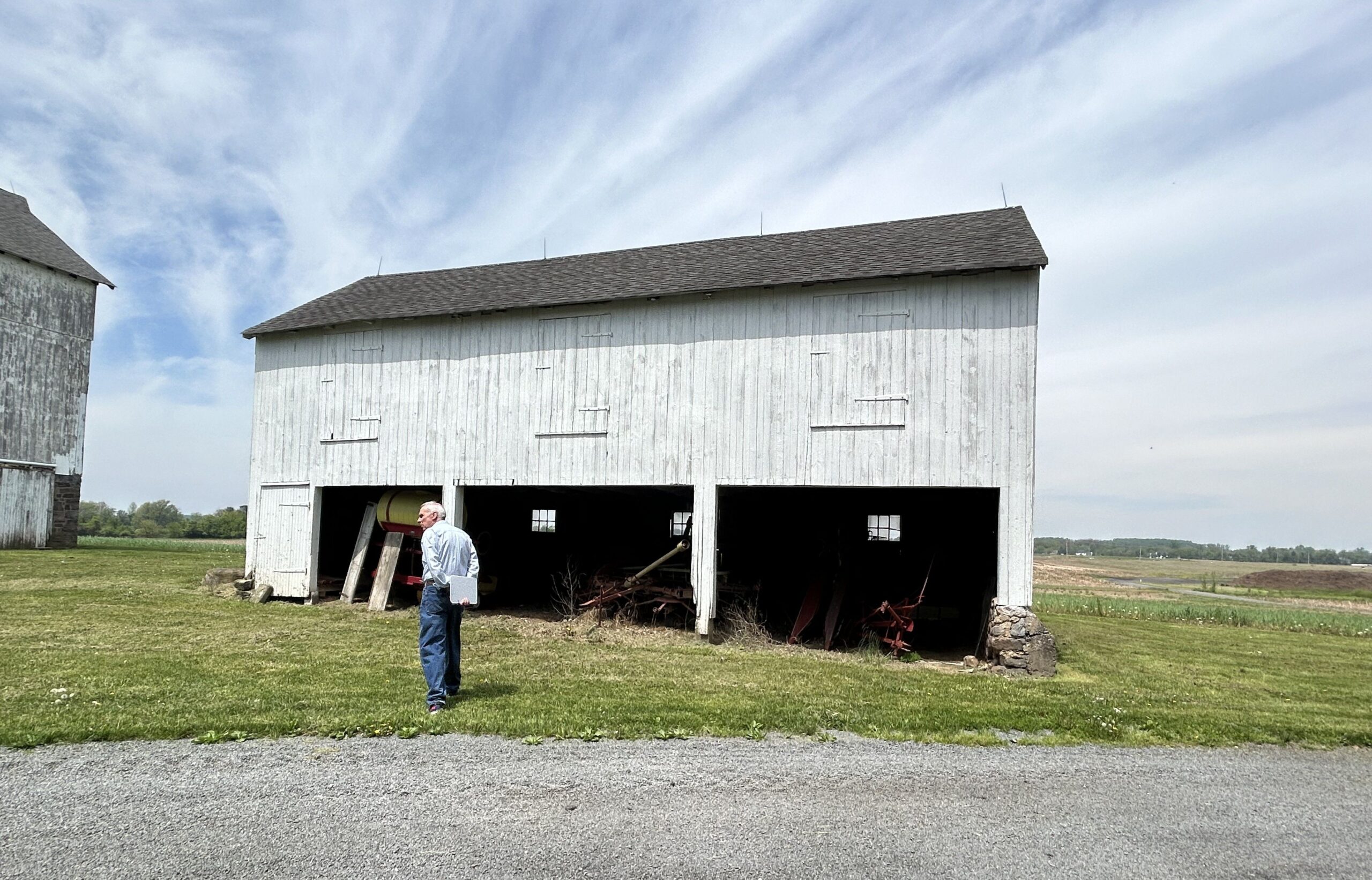 White man stands on grass in front of large barn.