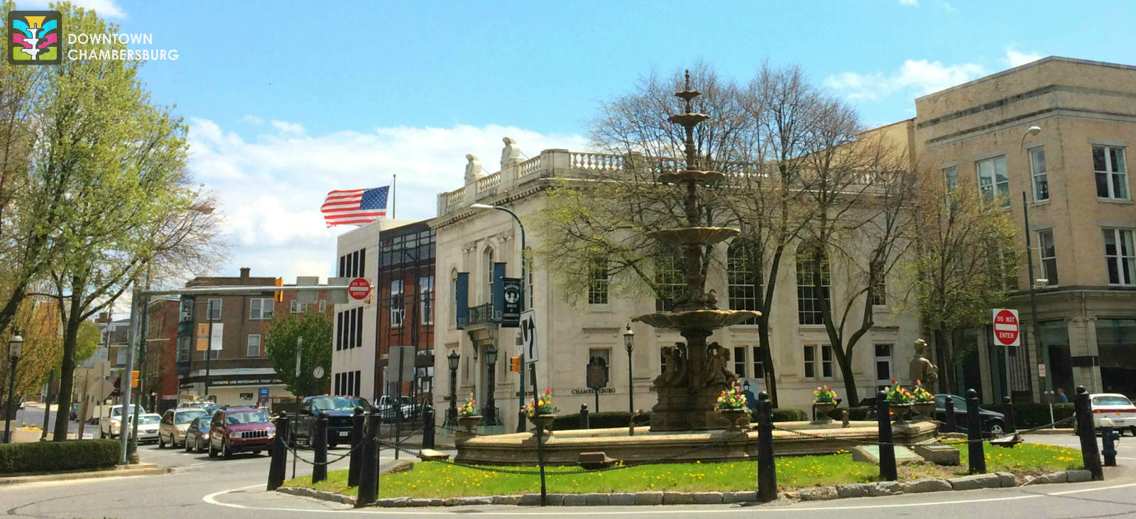 Collection of three story masonry buildings along busy streets and surrounding a large fountain in the center.