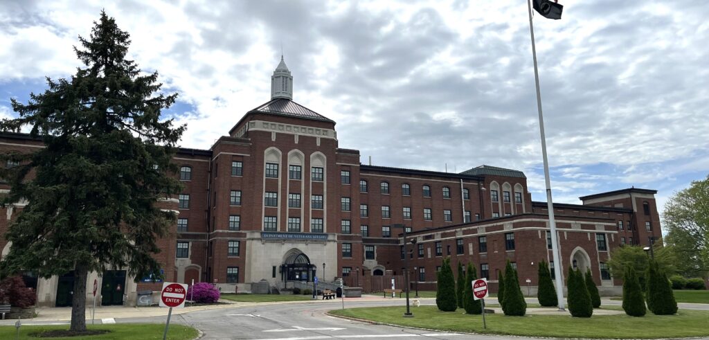 Very large, five-story brick building with large center entrance and wings to each side.
