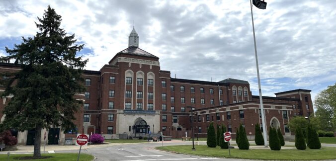 Very large, five-story brick building with large center entrance and wings to each side.