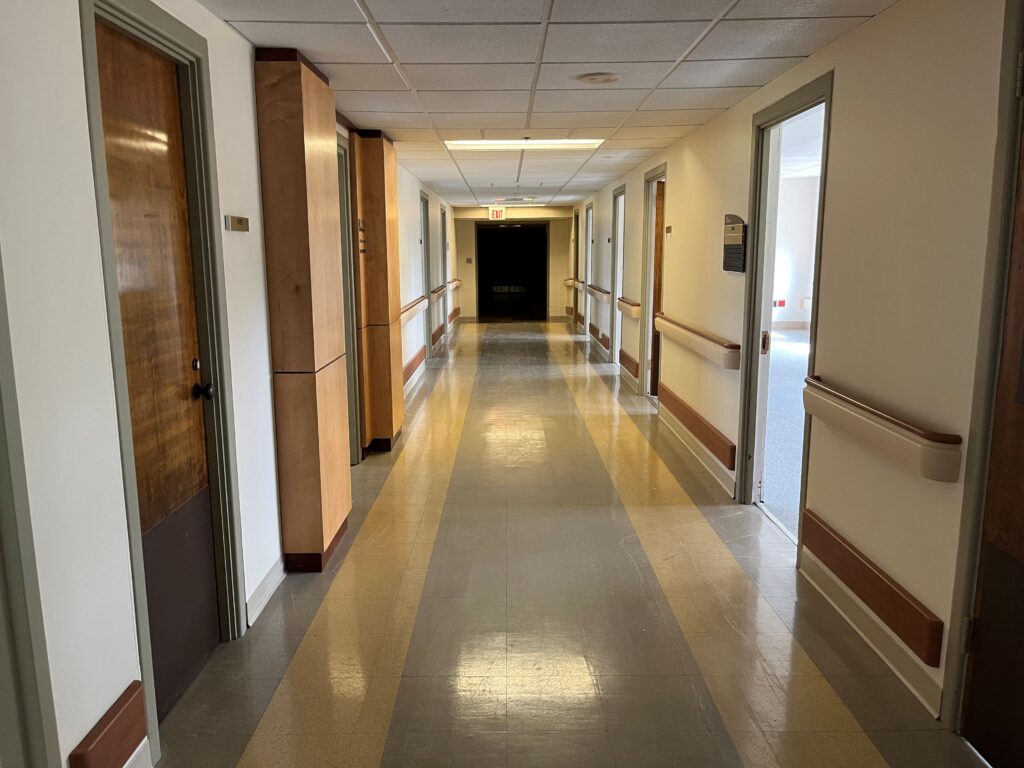 Hallway with linoleum floor, open and closed doors, and low ceiling.