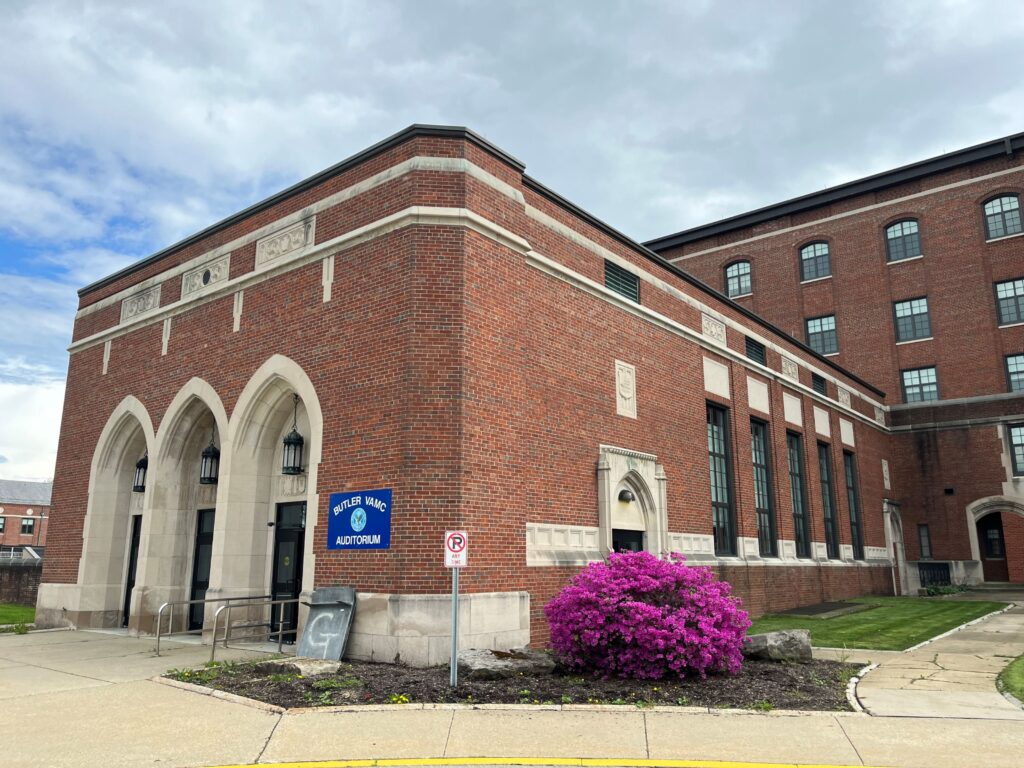 Rectangular brick building with flat roof, three entrance doors at front and windows along the side, with stone details.
