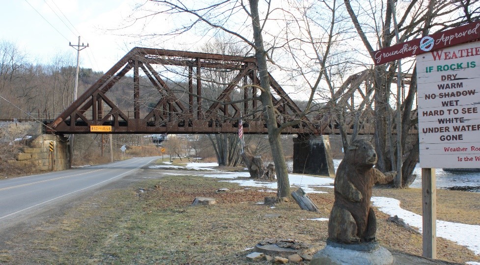 Large metal bridge over paved road and grass surrounded by trees and signage.