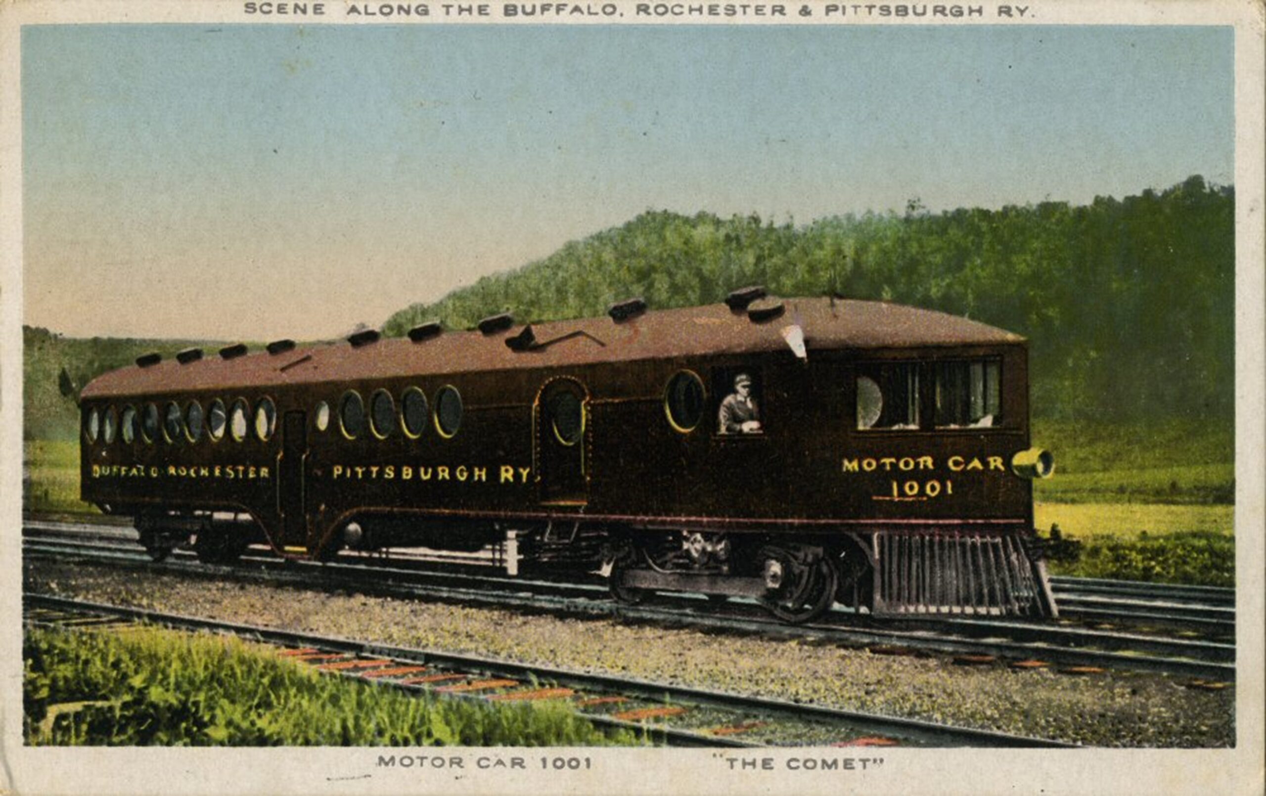 Long train engine with many circular windows on a track with trees in the distance.