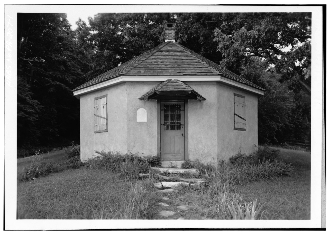 Small octagonal building with door, two windows, and conical roof.