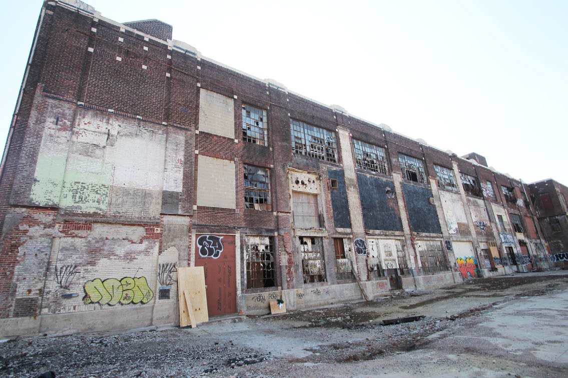 Brick industrial building with very large broken metal windows and graffiti in an urban setting.