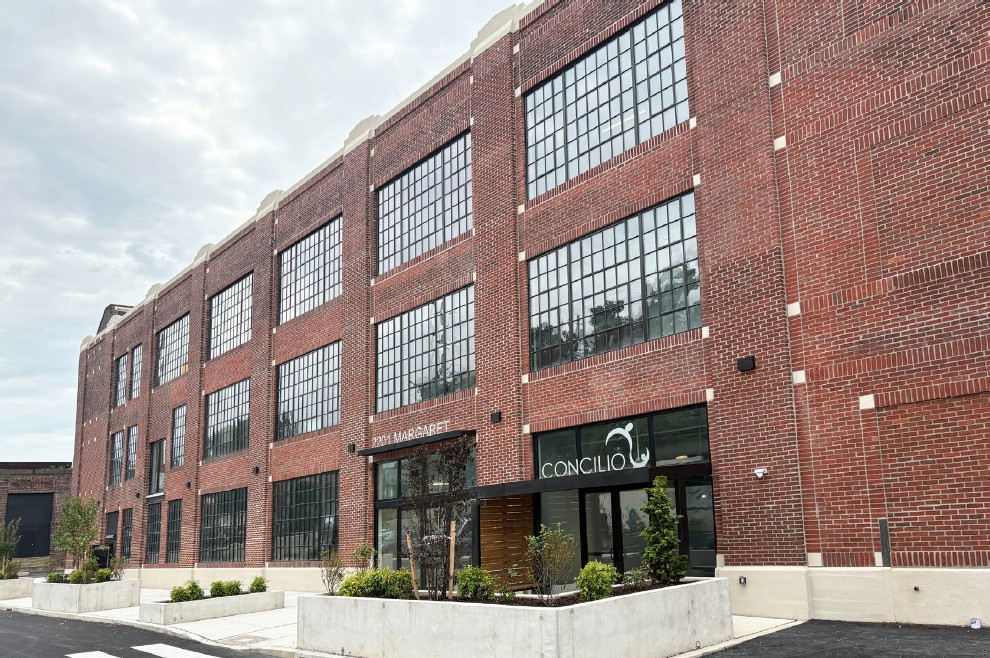 Brick industrial building with very large metal windows and entrance in parking lot.