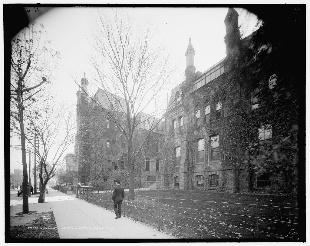 Historic photograph of two large brick buildings covered in ivy in an urban setting.