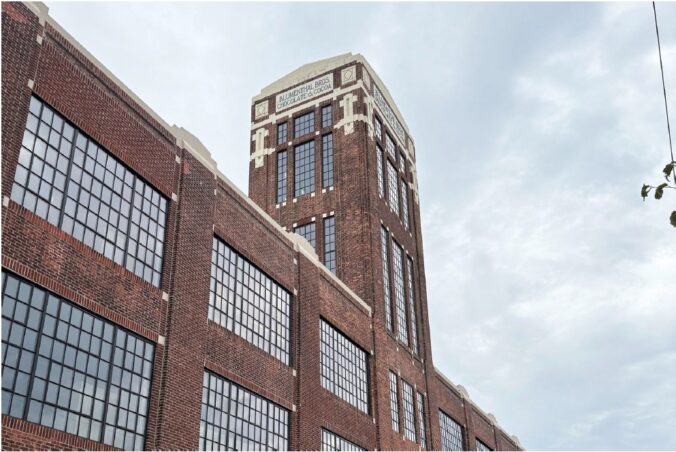 Brick industrial building with very large metal windows and a tall tower with windows.