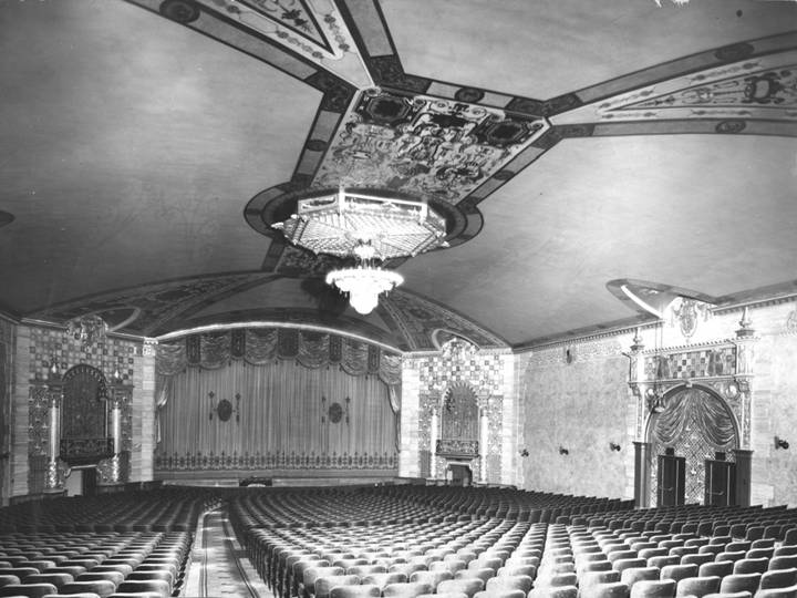 Black and white photograph showing the elaborate interior of a theater with seating, stage, lights, and painted details.