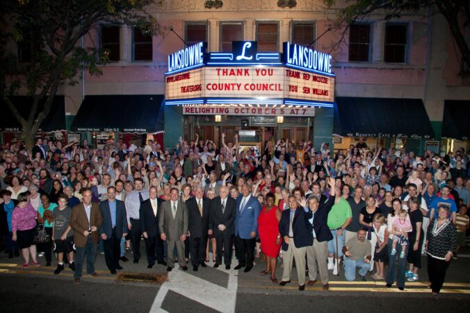 Large group of people stand outside theater building.
