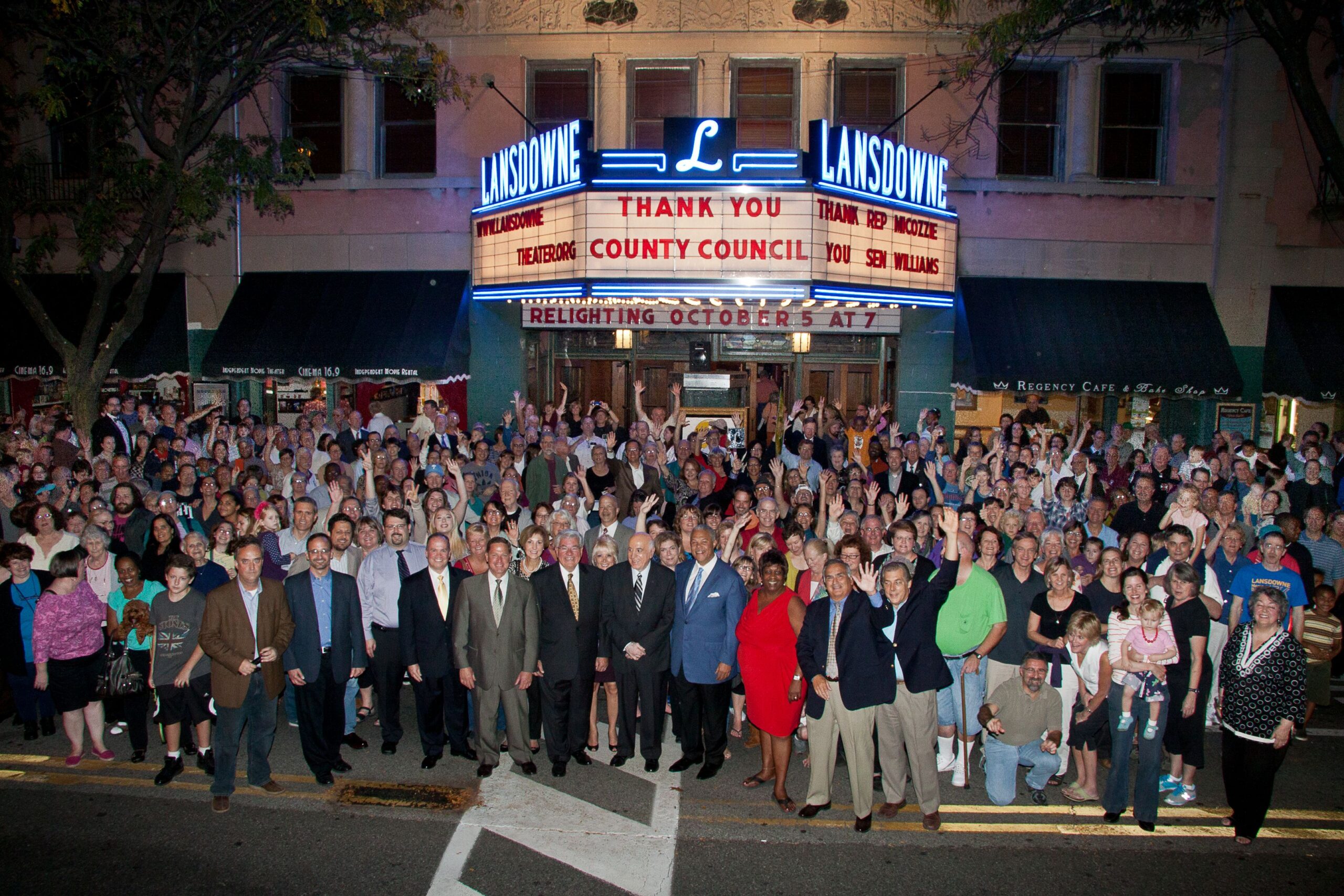 Large group of people stand outside theater building.