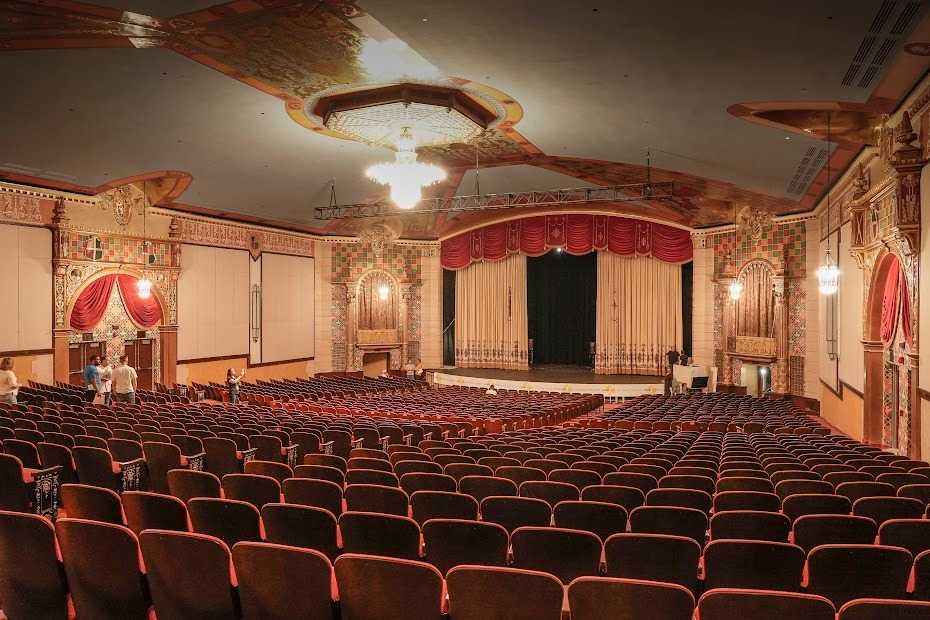 Eaborate interior of a theater with seating, stage, lights, and painted details.
