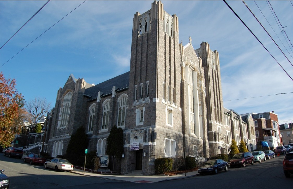 Large stone church in an urban area with cars parked along the street.